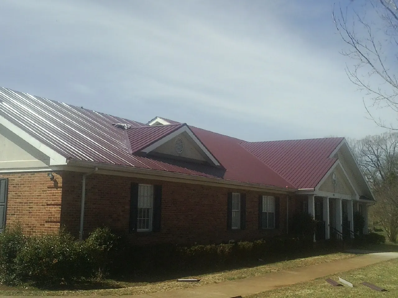 Red metal roof with gabled entries on a long brick building, from a Hail Damage Roof Repair job in Telford