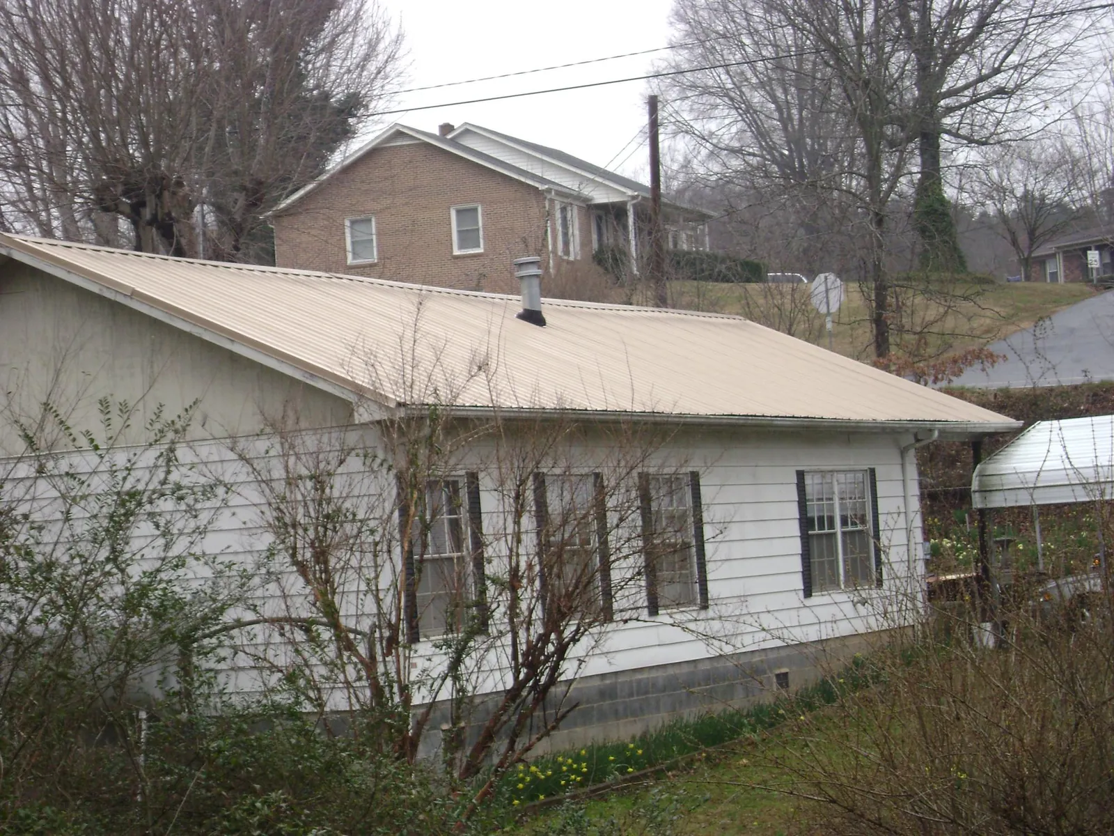Tan metal roof on a white sided house set into a hillside — Commercial Roofing by Roofing Brothers in Telford