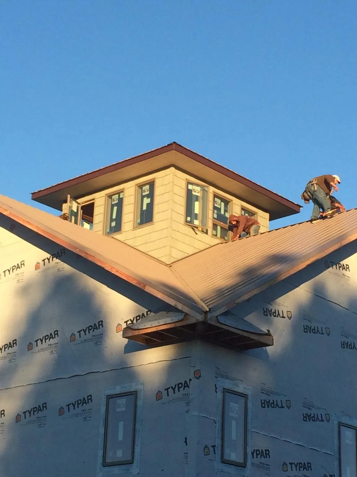 Roofers working around a rooftop cupola on a new metal roof at sunset — Roof Waterproofing in Telford by Roofing Brothers
